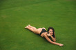 Young sexy and beautiful brunette fitness girl in black swimsuit posing turning booty shows ass at the green grass of Golf club. Sexy model portrait with perfect body. Concept of summer holiday