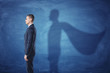 © gearstd - Businessman is standing in profile casting a shadow of the superman's cape on blue chalkboard background