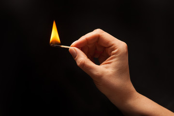 Woman hand holding lighted match, on black background.