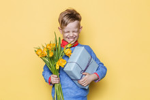 Handsome Boy Holding Flower Bunch And Gift Box. Valentine's Day. Birthday. Mother's Day. Studio Portrait Over Yellow Background