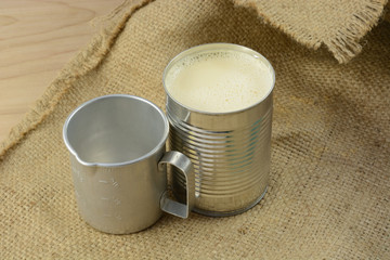 Canned evaporated milk and vintage retro measuring cup on burlap