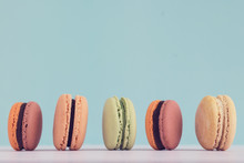 Raw Of Pastel Colors Assorted French Macaroons On A Blue Colored Background. Copy Space For Text. Horizontal