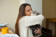 Loving girl huging her cat at home near the window. Cheerful girl kissing her pet in a domestic clothes. Girl loves her cat. Friends expressing feelings