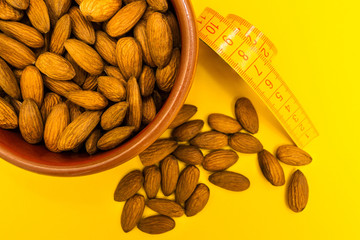 Wall Mural - Almonds in a plate near the measuring tape on a yellow background, diet.