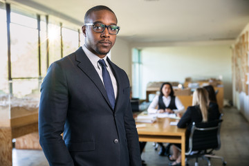 Confident african american lawyer standing strong with legal team meeting in background