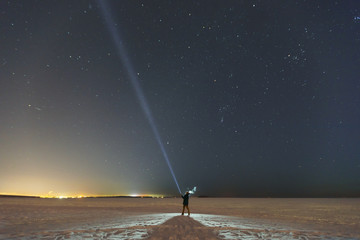 silhouette of a man with a flashlight, observing beautiful, wide blue night sky with stars and visib