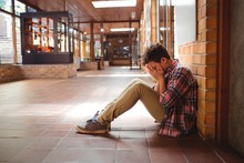 Sad Schoolboy Sitting Alone In Corridor