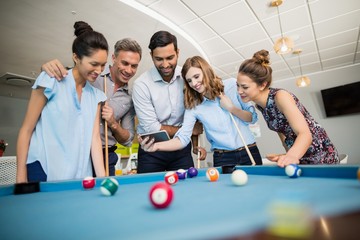 Wall Mural - Colleagues using phone while playing pool in off