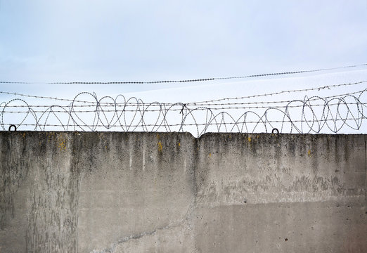 Fototapete - Concrete wall, against the backdrop of barbed wire, the concept of prison, salvation, Refugee, lonely, space for text, free