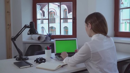 Poster - Woman working with computer in office or at home. Lady with long blond hair sitting at the desk typing on keyboard. Designer looking on the green screen laptop.