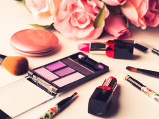 Make up products lipstick, blush eye shadows and tools brushes with pink roses flowers on white background. Lifestyle woman still life