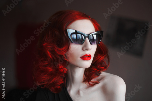 A Woman With Her Red Curly Hair In A Black Dress And Fox Glasses On A
