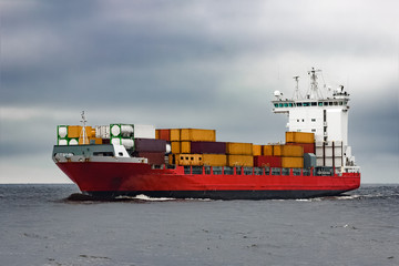 Red cargo container ship sailing from Baltic sea in cloudy day