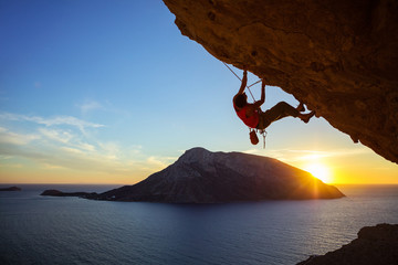 Wall Mural - Young man climbing overhanging cliff at sunset