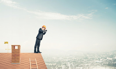 Engineer man standing on roof and looking in binoculars. Mixed m