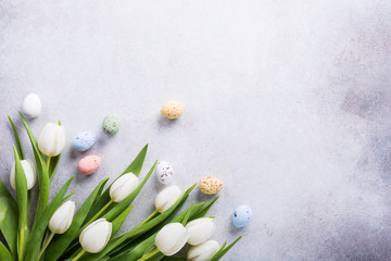 Wall Mural - Beautiful white tulips with colorful quail eggs on light gray stone background. Spring and Easter holiday concept with copy space.