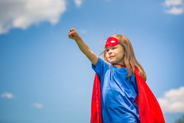 Funny little girl playing power super hero over blue sky background. Superhero concept.