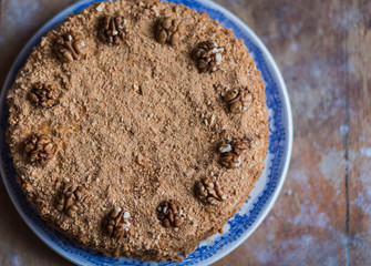 Wall Mural - round delicious honey cake in blue white plate on light brown wooden background with flour