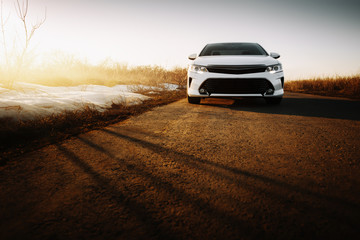 Wall Mural - White modern car at asphalt road at sunset