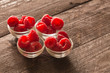 raspberries in small bowls on a wooden background.
