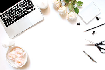 Minimalistic feminine workplace with laptop keyboard, pen, white candles, notebook, office clips and roses in flat lay style. White background, top view, frame