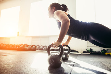 Gym woman push-up strength pushup exercise on kettlebells in a fitness workout. focus on kettlebells