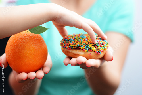 Zdjęcie XXL Dziecko otyłości pojęcie z małej dziewczynki ręką wybiera słodkiego i niezdrowego pączek zamiast owoc