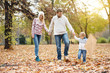 © chika_milan - Happy family walking in park through the fallen leafs, they are holding hands