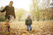 © chika_milan - Mother and son having good time kicking fallen leafs in the park
