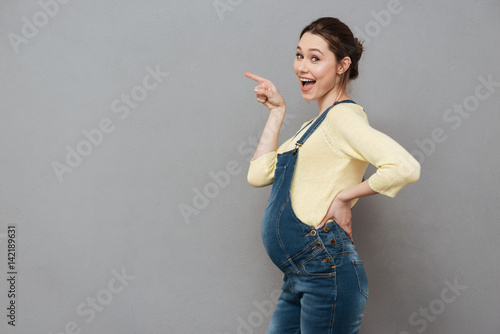 Cuadros en Lienzo Cheerful smiling pregnant lady pointing.