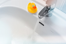Water Running From A Faucet Into A White Sink With A Rubber Duck On The Side