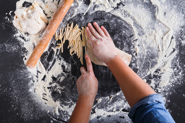 Canvas Print - Cooking noodles concept on black background, sprinkled flour