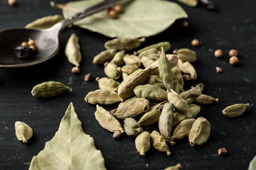 Cardamon dry seeds and laurel leafs on a black wooden table, closeup shot