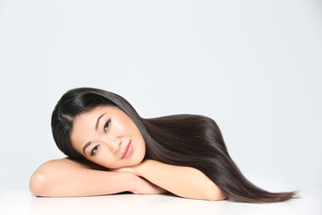 Wall Mural - Beautiful Asian woman with long straight hair on light background