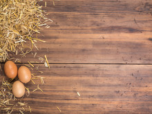 Rural Eco Background With Brown Chicken Eggs And Straw On The Background Of Old Wooden Planks. The View From The Top. Creative Background For Easter Cards, Menu Or Advertising