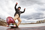 Teen skater in a hoodie sweatshirt and jeans slides over a railing on a skateboard in a skate park