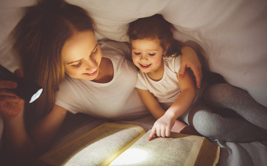 Mother and child read book under blanket with a flashlight.