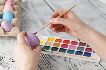 Wall Mural - Woman painting Easter eggs, on white wooden background