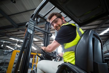 Wall Mural - Portrait of smiling factory worker driving forklift