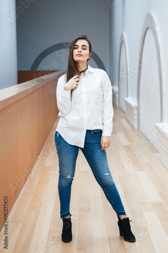 Portrait Of Sexy White Caucasian Brunette Young Beautiful Girl Woman Model With Long Dark Hair In White Shirt And Blue Jeans Indoor In Hall At College University Standing Full Figure Stock Photo Portrait Of Sexy White Caucasian Brunette Young Beautiful Girl Woman Model With Long Dark Hair In White Shirt And Blue Jeans Indoor In Hall At College University Standing Full Figure Stock Photo