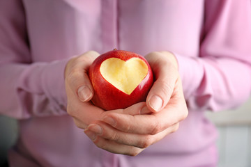 Wall Mural - Woman hands holding fresh red apple with heart-shaped cut out, closeup