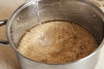 Wall Mural - Pouring water into pan with brown rice, closeup