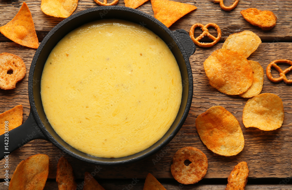 Frying pan with creamy cheese, chips and crackers on wooden background