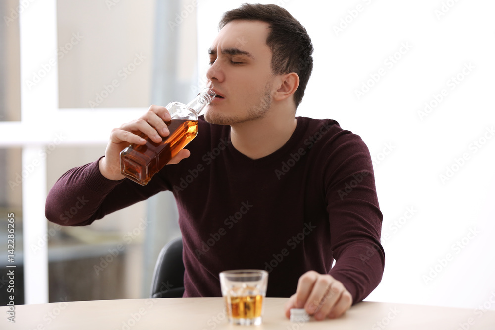 Handsome depressed man drinking whisky at home