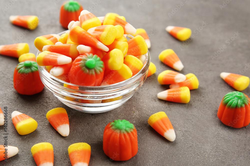 Bowl with tasty Halloween candies on textured background