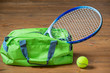 A tennis racket sticks out of a green sports bag, objects on the floor