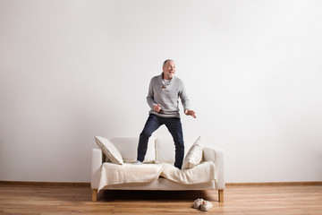 Wall Mural - Handsome senior man standing on couch, dancing. Studio shot.