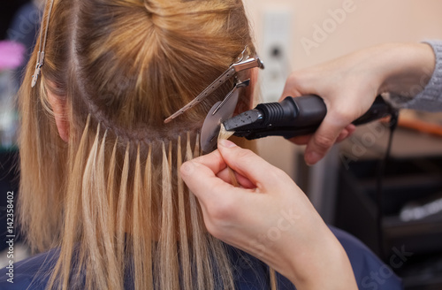 Fotomural The hairdresser does hair extensions to a young girl, a blonde in a beauty salon