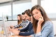 © W PRODUCTION - portrait of beautiful and cheerful young woman telephone operator with headset working on desktop computer in row in customer service call support helpline business center