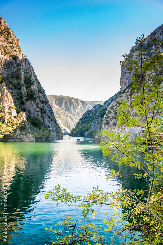 View of beautiful tourist attraction, lake at Matka Canyon in the Skopje surroundings, Macedonia. Branch with leafs in the foreground, vertical composition. - obrazy, fototapety, plakaty 